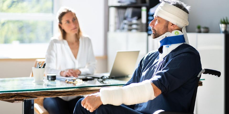 Advogada conversando com um cliente de braço engessado, em cadeira de rodas