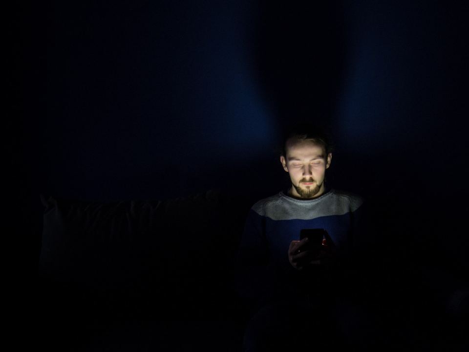 Homem no escuro, com o rosto iluminado pela tela do celular