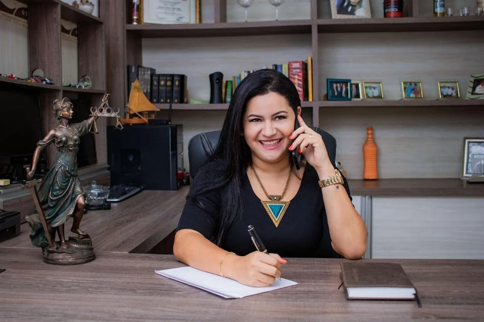 Advogada sorrindo ao telefone, anotando numa mesa de escritório
