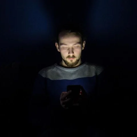 Pessoa no escuro, com o rosto iluminado pela tela do celular