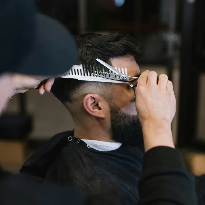Barbeiro cortando o cabelo de um cliente com o pente e a tesoura