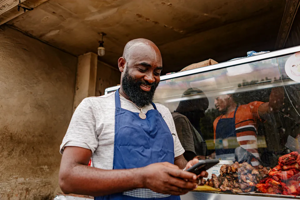 Dono de um restaurante, de avental, sorrindo para o celular